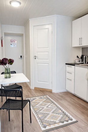A kitchen with white cabinets, a dining table with chairs, a rug, and a door with a no smoking sign.