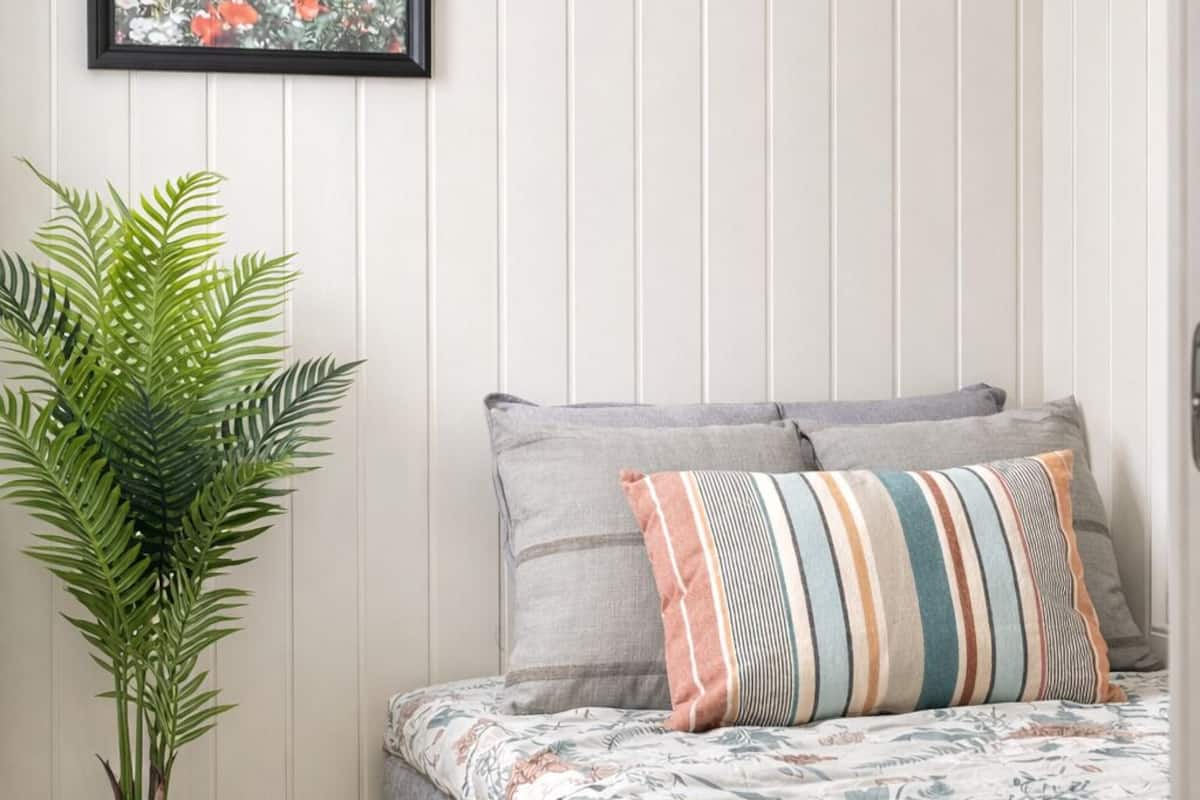 A bedroom with a bed, pillows, a framed picture, and a potted plant.