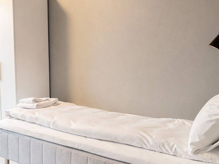 Een eenpersoonsbed met een grijs hoofdbord en een witte matras in een kamer met neutrale kleuren.