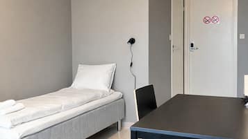 A room with a bed, a table, and a door with a no-smoking sign.