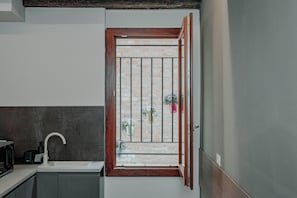 A kitchen with a white sink, a wooden-framed window with metal bars, and a view of a brick wall with hanging plants. - Casa Loredana (Venice)