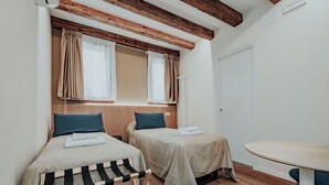 Quarto com duas camas, teto de madeira, uma mesa redonda e uma porta branca.