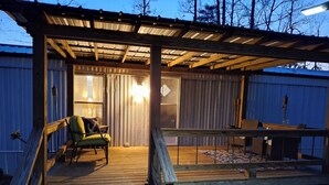 Een overdekt terras met een stoel en tafel, houten treden die naar een deur leiden, en een metalen reling.