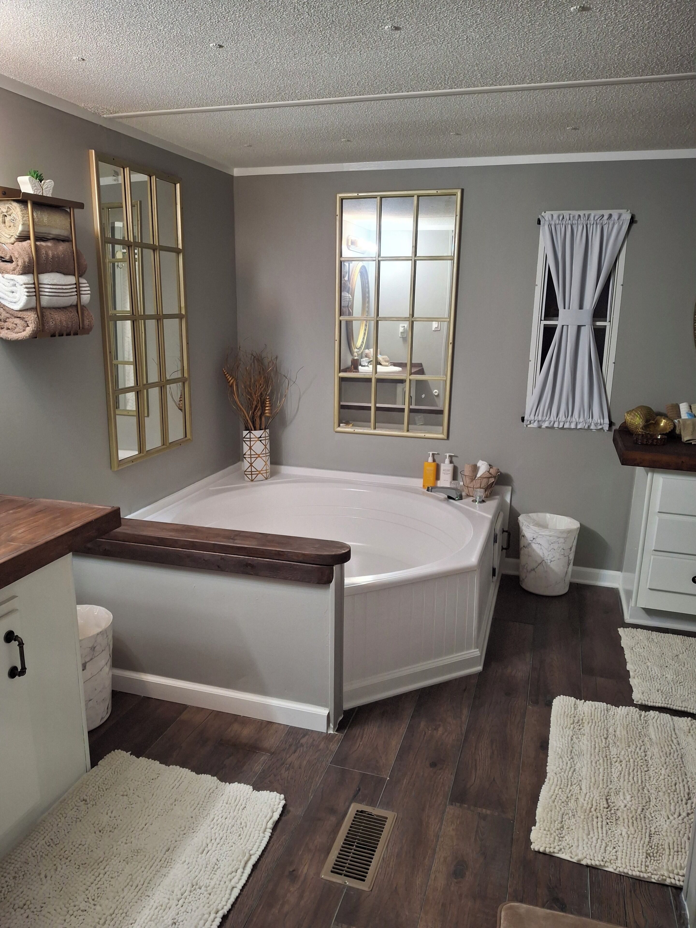 A bathroom with a bathtub, a vanity with a mirror, a window with curtains, and a towel rack with folded towels.