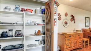 Una cocina con estantes blancos, armarios de madera y una zona de comedor con mesa y sillas de madera.