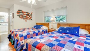 Un dormitorio con dos camas, un ventilador de techo, una ventana con persianas y un adorno en la pared.