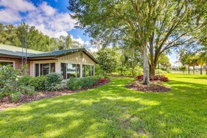 A house with a green roof, a covered porch, and a well-maintained lawn with trees and shrubs. - Lakefront Frostproof Retreat with Private Beach (Frostproof)