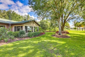 A house with a green roof, a covered porch, and a well-maintained lawn with trees and shrubs. - Lakefront Frostproof Retreat with Private Beach (Frostproof)