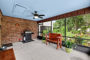 An outdoor patio with a brick wall, a grill, a wooden bench, and a view of a garden. - Lakefront Frostproof Retreat with Private Beach (Frostproof)
