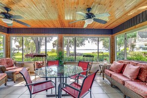 A sunroom with a glass table, red chairs, wicker sofas, and ceiling fans. - Lakefront Frostproof Retreat with Private Beach (Frostproof)