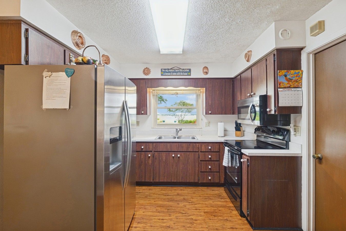 A compact kitchen with wooden cabinets, a stainless steel refrigerator, a window with a view, and a microwave.