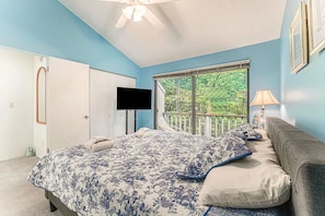 A bedroom with a bed, a TV, a window with a view of trees, a ceiling fan, and a nightstand with a lamp. - The Homestead Glen Arbor Condo Lake Michigan (Glen Arbor)