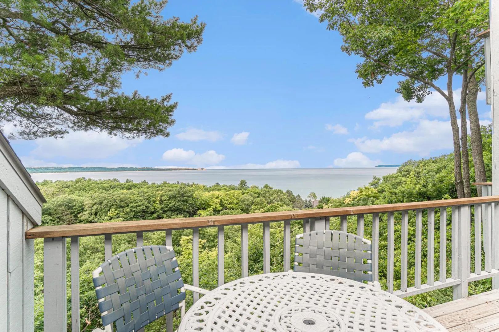 A deck with a table and chairs, overlooking a body of water and greenery.