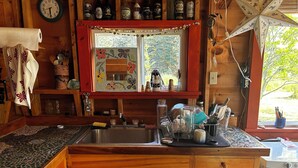 A wooden cabin kitchen with a sink, wooden cabinets, a clock, and various kitchen items. - 1-Bedroom Off Grid Cabin on Remote Island Across from Acadia National Park (Tremont)
