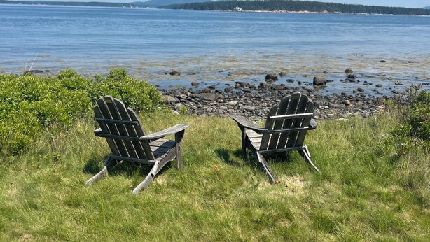 Two Adirondack chairs facing a lake with a rocky shoreline and distant mountains. - 1-Bedroom Off Grid Cabin on Remote Island Across from Acadia National Park (Tremont)