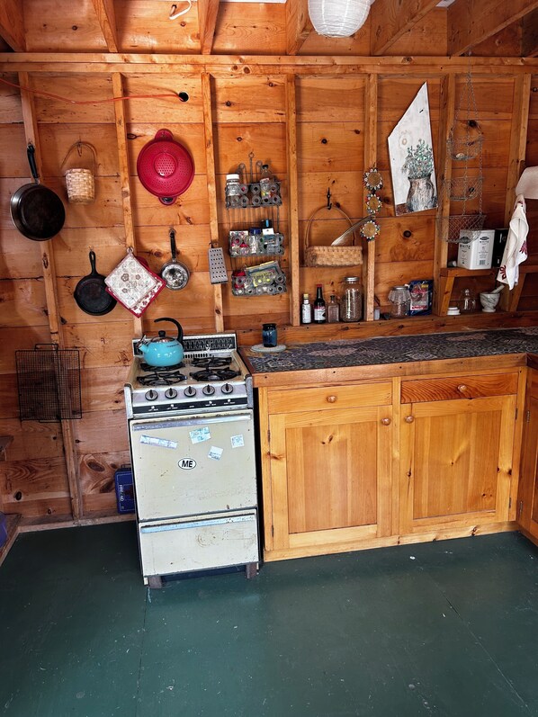 A rustic kitchen with wooden walls, a gas stove, a white oven, and various kitchen utensils and containers on the wall.
