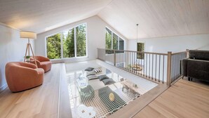 A spacious loft with a high ceiling, large windows, a wooden floor, and a balcony with a railing.