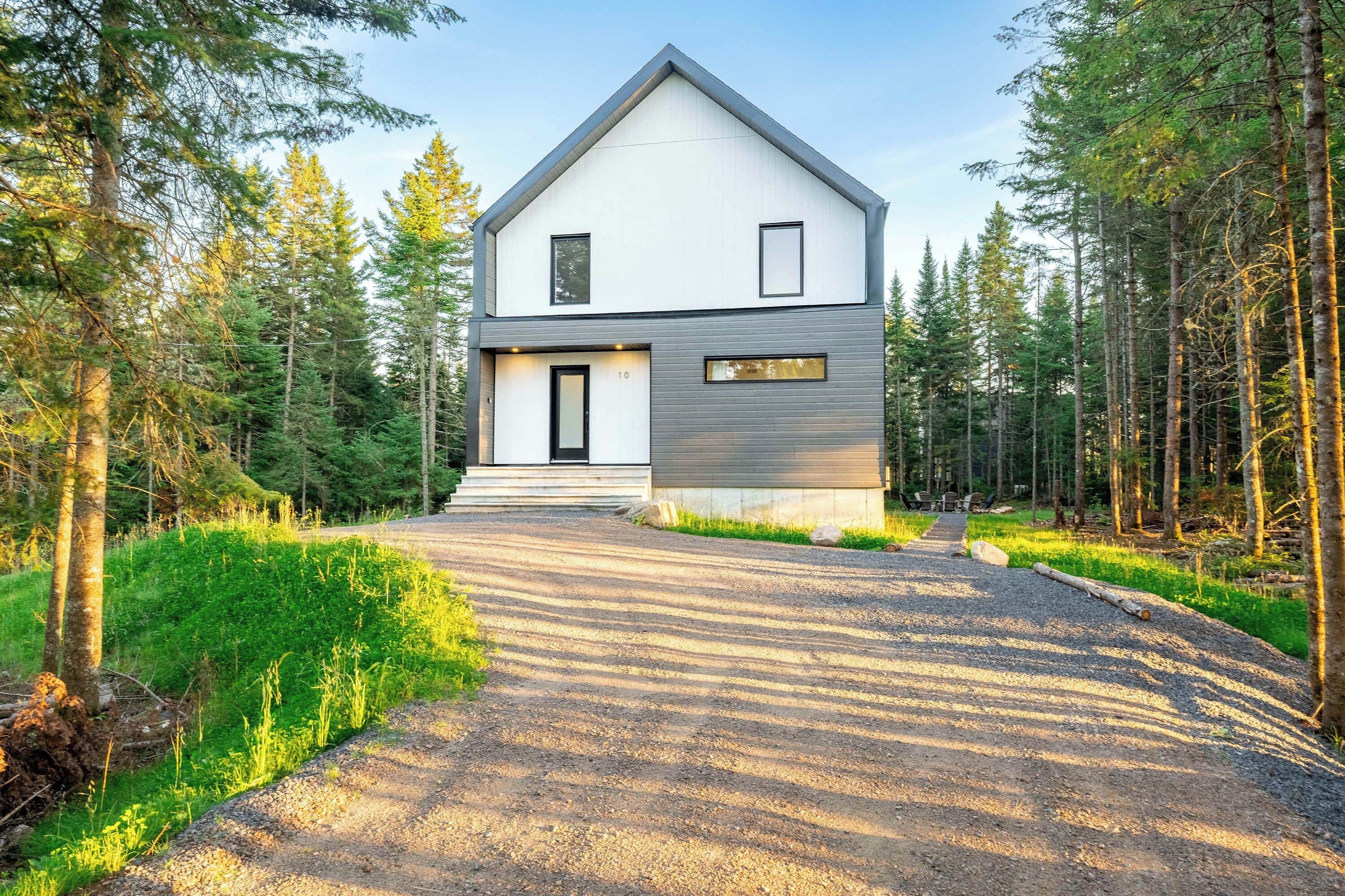 Une maison moderne à deux étages, avec une allée en gravier menant à une porte en bois.