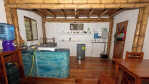 Una cocina con dispensador de agua, lavamanos, refrigerador y una mesa de madera con sillas.