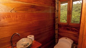 Un baño de estilo cabaña de madera con lavamanos de madera, inodoro y ventana.