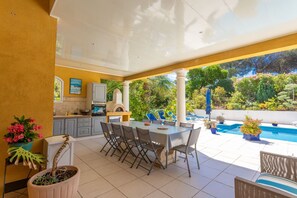 An outdoor patio with a dining table, chairs, a pool, and a kitchen area. - Room "Le Petit Ramsès - Hortensia" with Shared Pool, Wi-Fi and Air Conditioning (Sainte-Maxime)