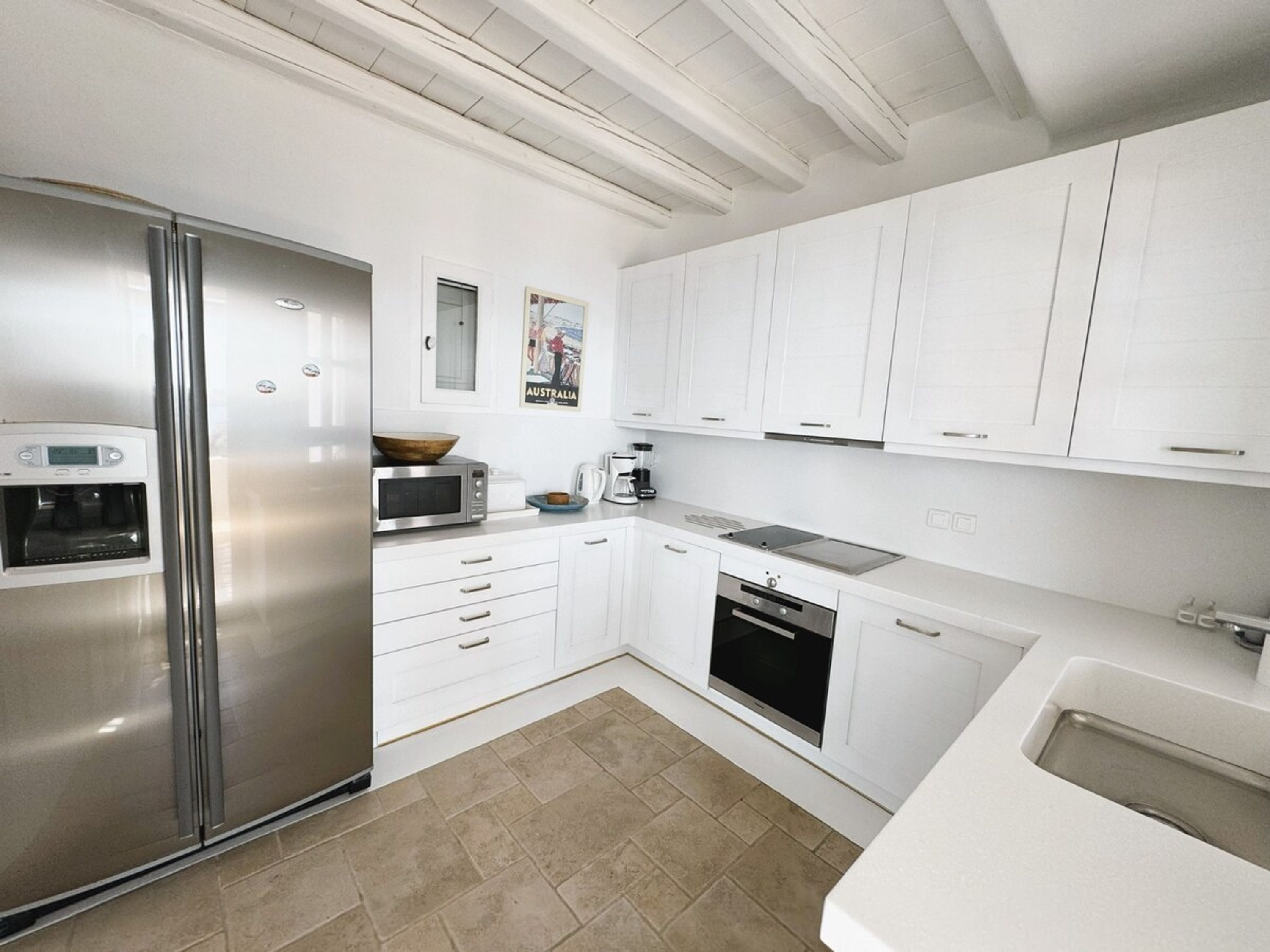 A modern kitchen with white cabinetry, a stainless steel refrigerator, a microwave, a coffee maker, and a dishwasher.