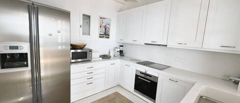 A modern kitchen with white cabinetry, a stainless steel refrigerator, a microwave, a coffee maker, and a dishwasher.