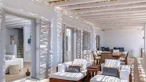 A sunlit room with a sofa, armchairs, and a dining table. - Luxury Villa Roshell (Mykonos)