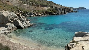 A coastal landscape with clear turquoise water, rocky shorelines, and a hilly backdrop. - Luxury Villa Roshell (Mykonos)
