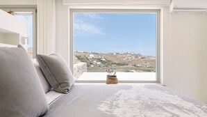Ein Schlafzimmer mit großem Fenster, einem Bett und Blick auf eine hügelige Landschaft.
