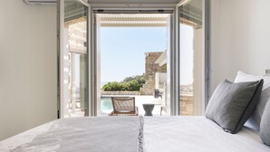 Ein Schlafzimmer mit einem großen Bett, Blick auf einen Pool und ein Steinhaus im Hintergrund.