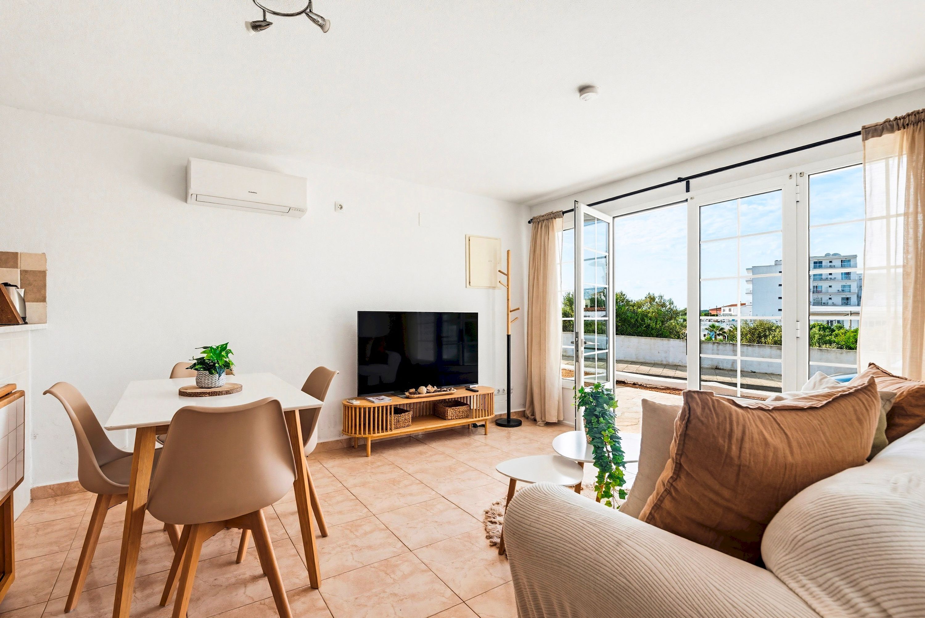 A living room with a TV, dining table, chairs, sofa, and large windows.