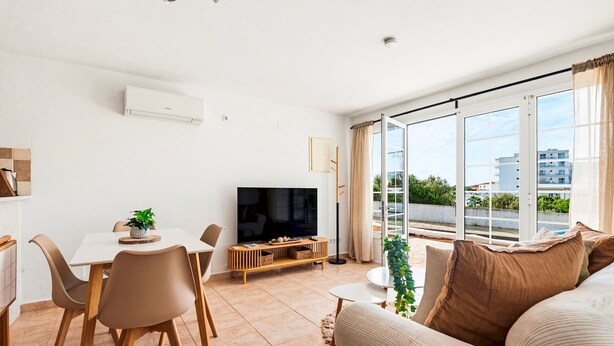 Een woonkamer met een televisie, eettafel, stoelen, bank en grote ramen.
