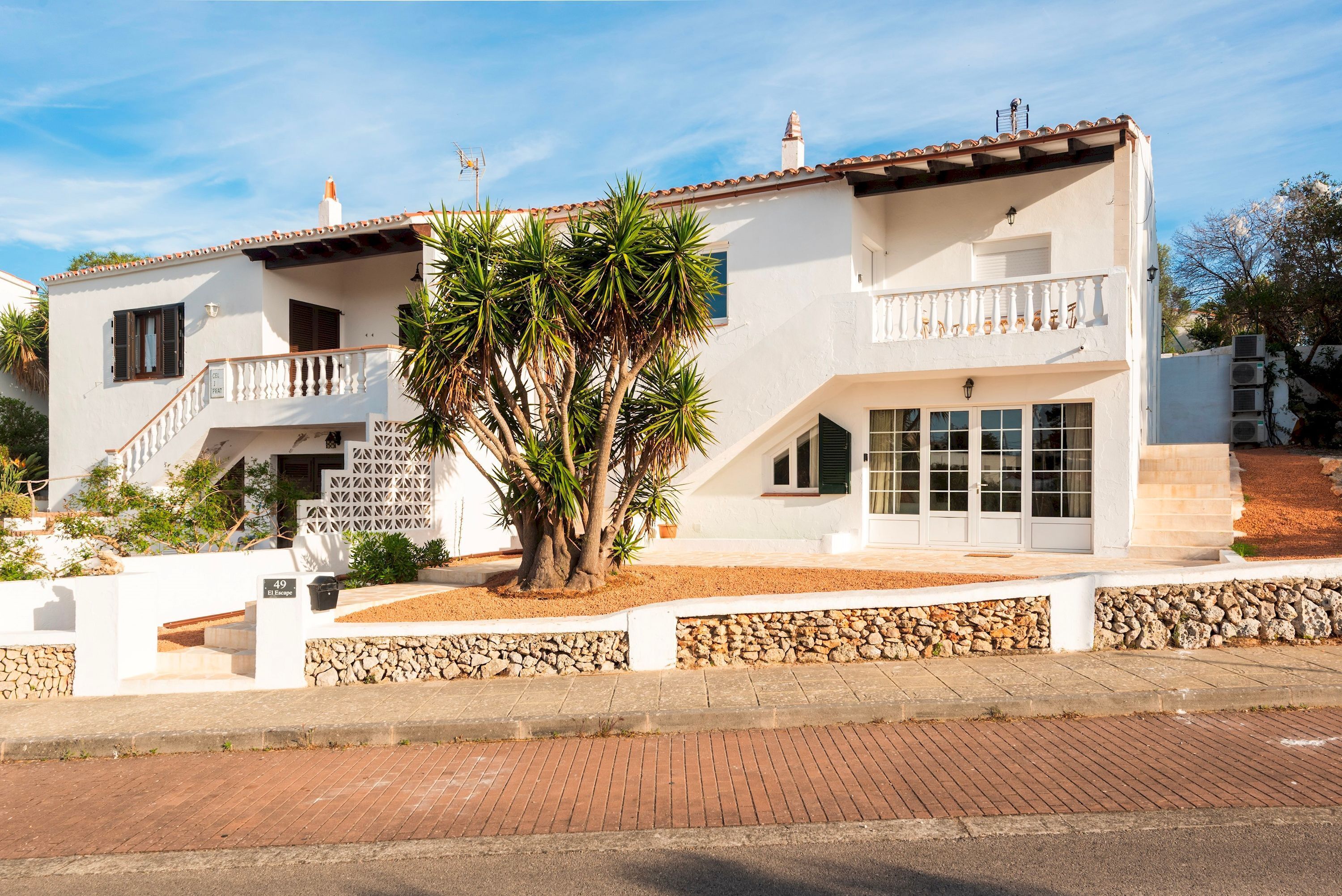 A two-story building with a white facade, a balcony, and a stone wall in front.