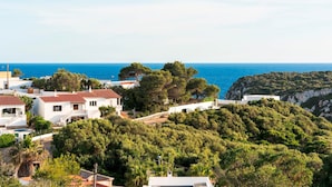 Un pueblo costero con edificios blancos, vista al mar y una colina con vegetación densa.