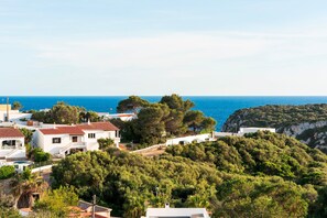 A coastal village with white buildings, a view of the sea, and a hill with dense greenery. - El Escape - Terrace and swimming pool - Menorca (Minorca)