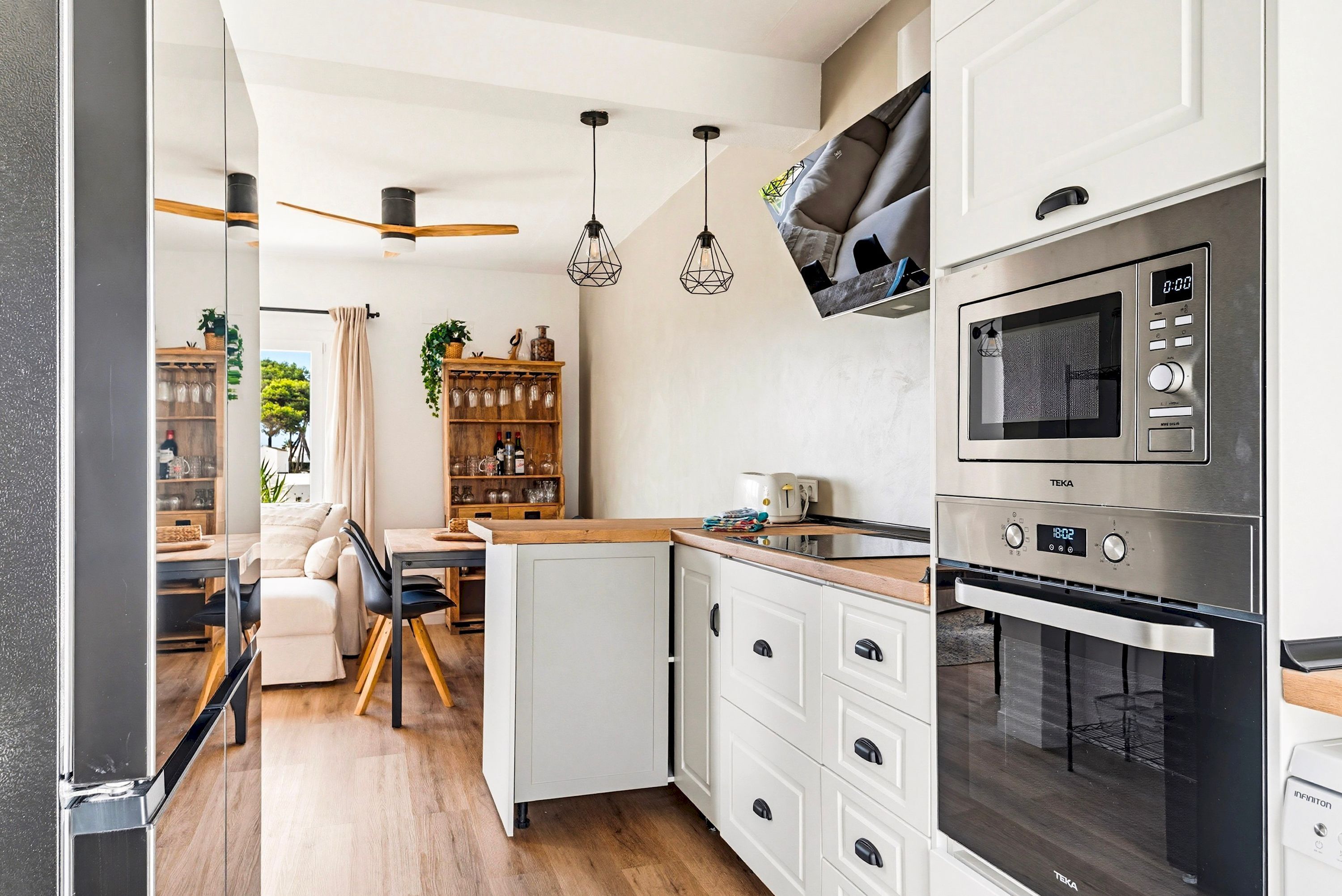 A modern kitchen with white cabinets, a built-in oven, a microwave, and pendant lights.