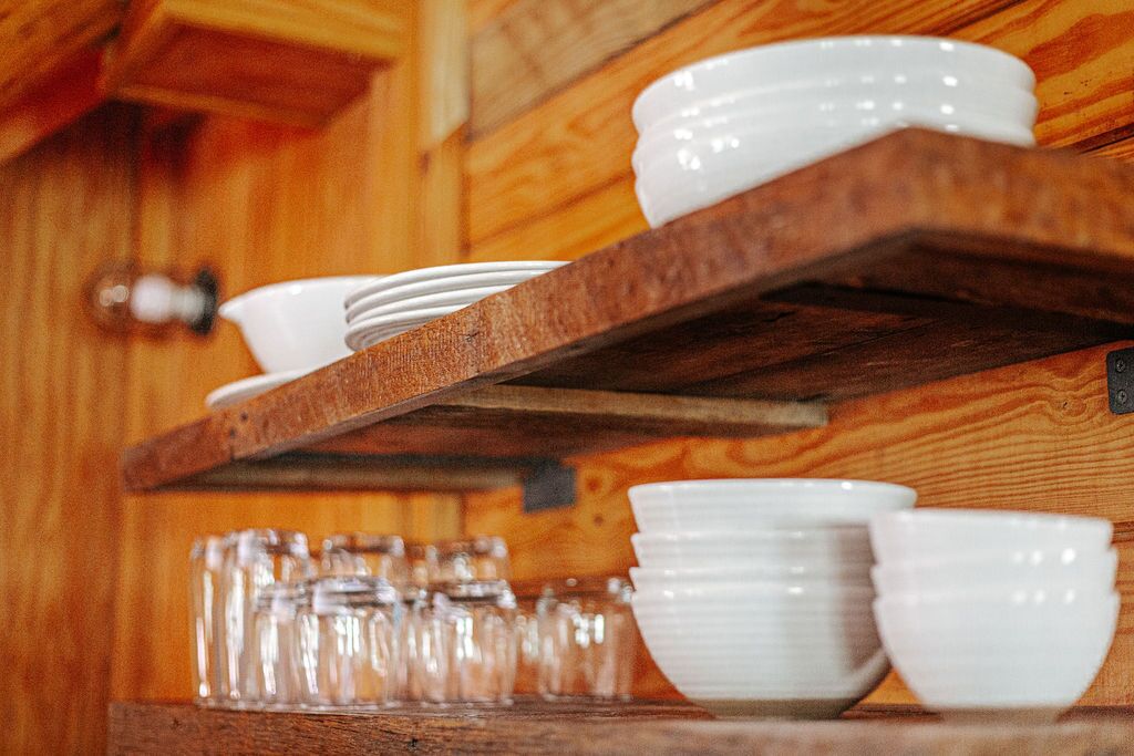 A wooden shelf with white bowls and glasses.