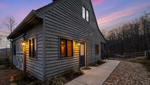 A wooden cabin with a sloped roof, a front porch, and a pathway leading to the entrance. - Blue's Barn (Nellysford)