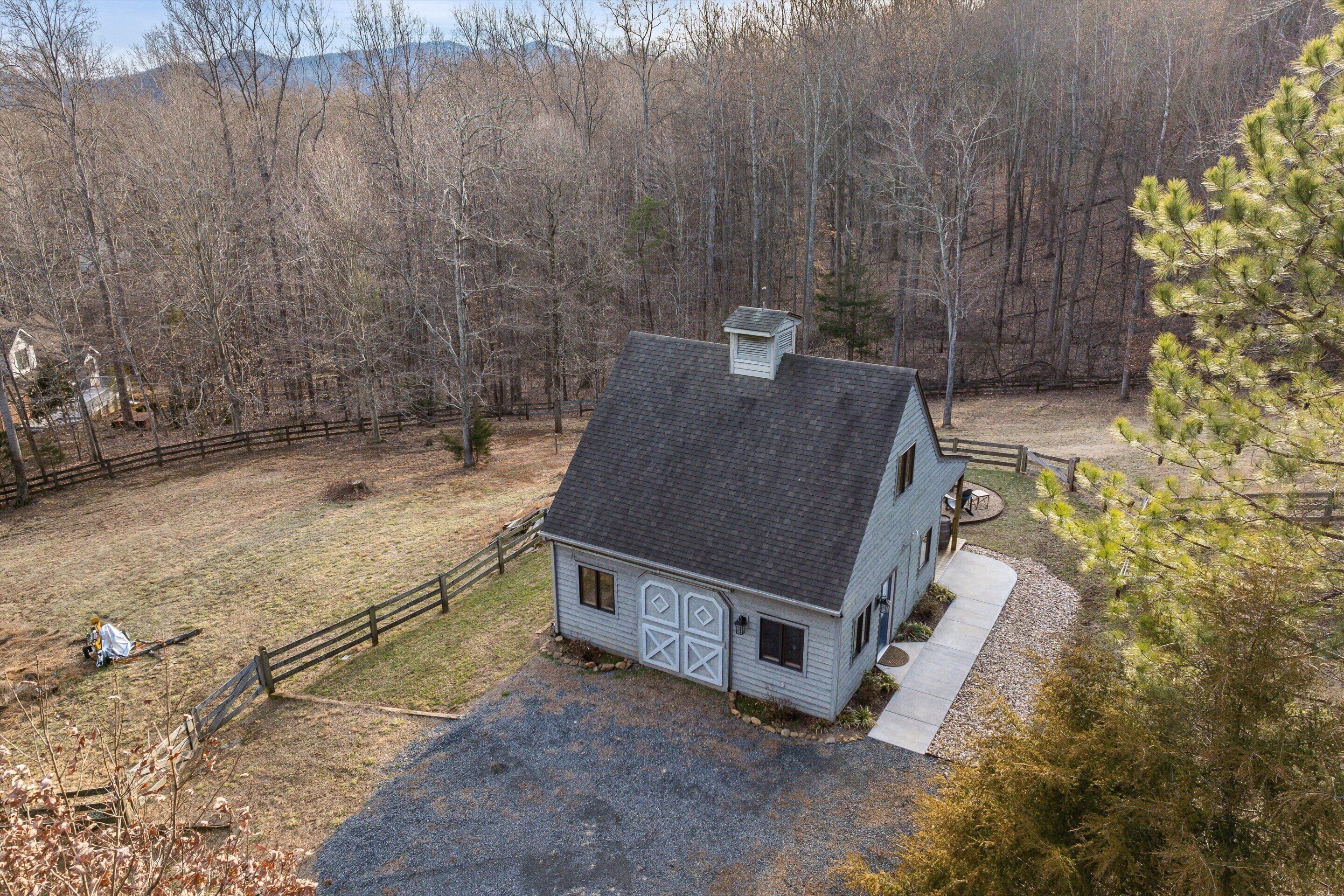 A small, single-story house with a dark roof and light siding, surrounded by a wooden fence and a gravel driveway.