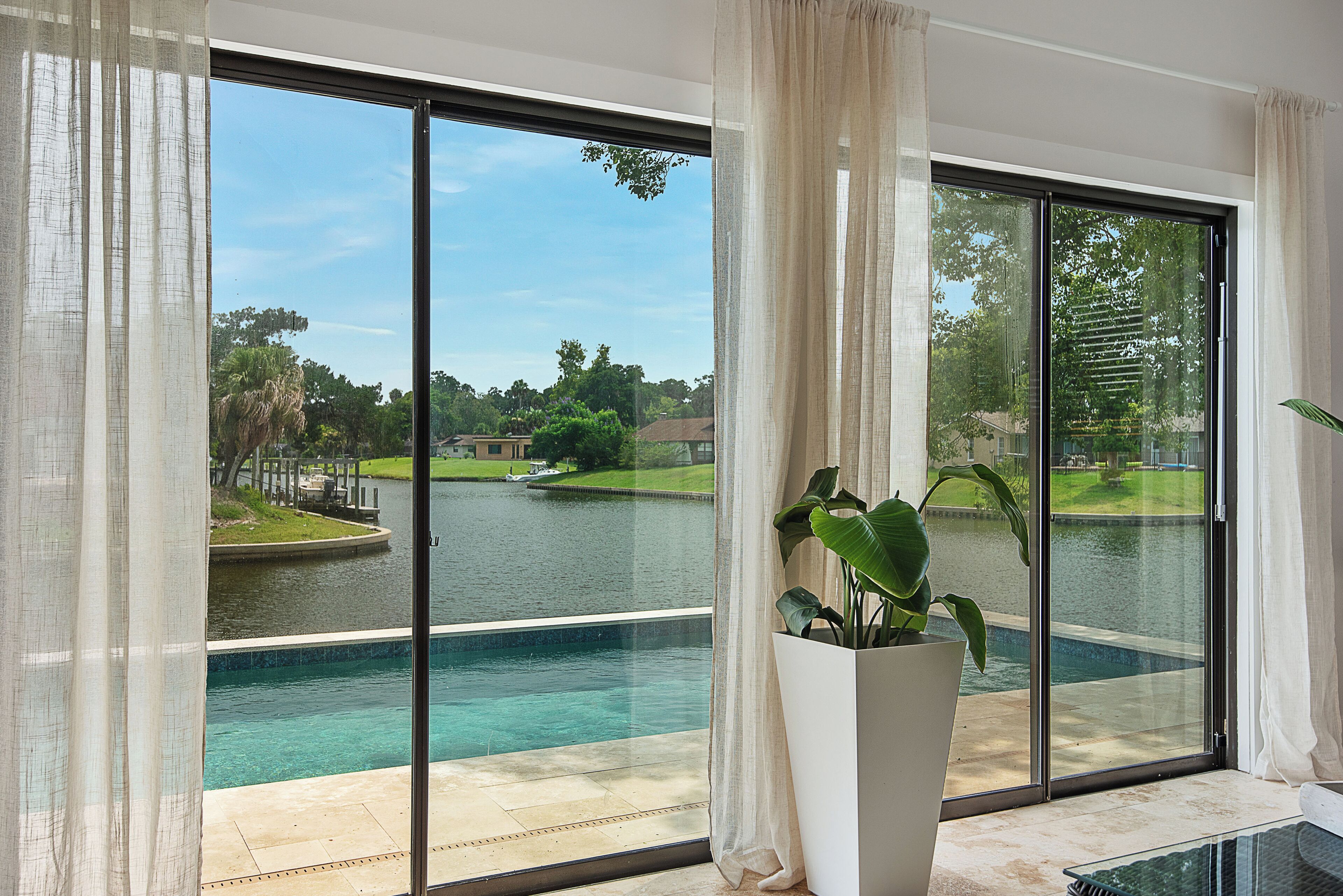 Ein Zimmer mit einer großen Schiebeglasdoor zum Pool, einer Topfpflanze und Blick auf einen See mit Golfplatz.