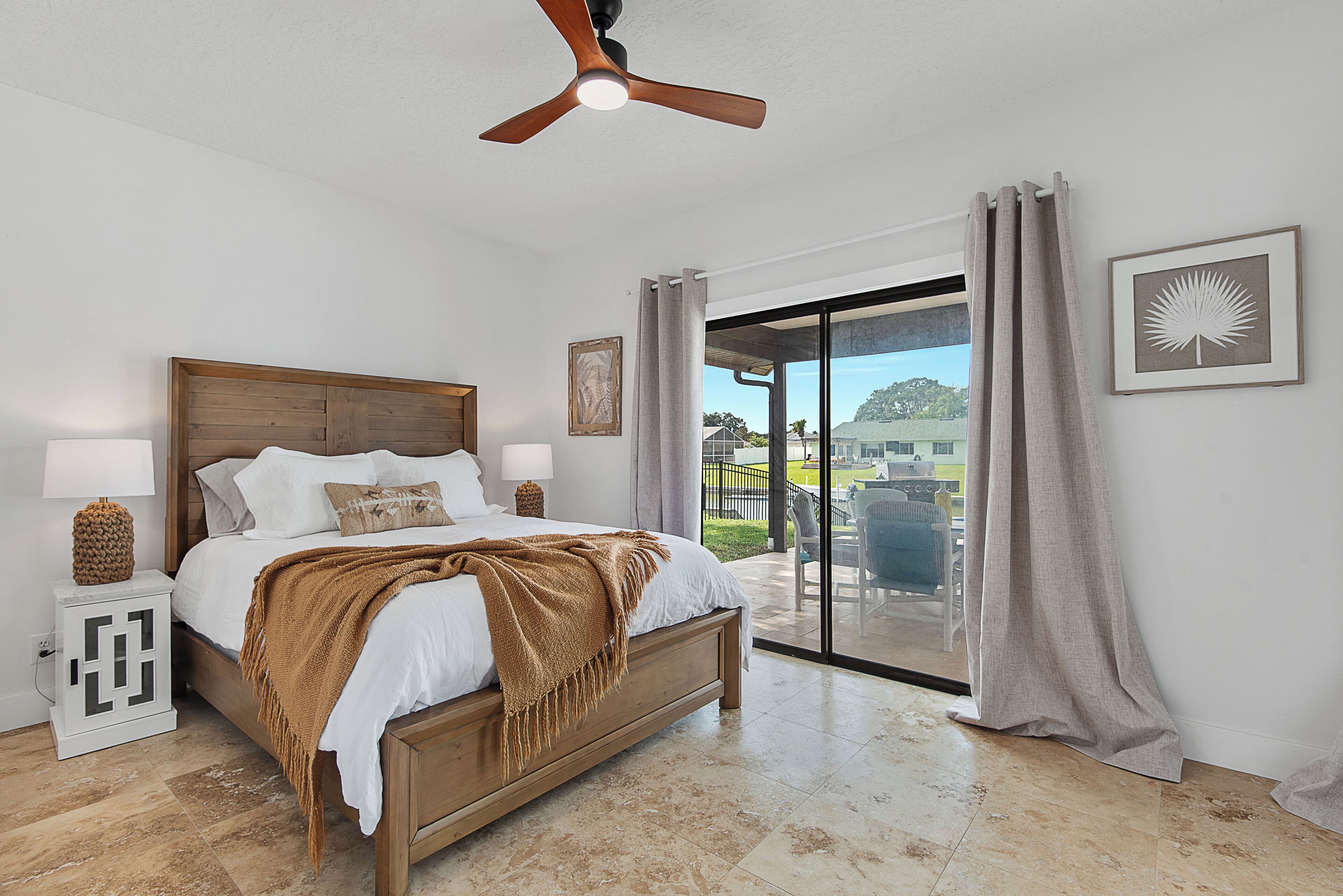 Une chambre à coucher avec un lit, des lampes de chevet, un ventilateur de plafond, une fenêtre avec des rideaux et une vue sur l’extérieur.