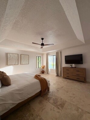 Ein Schlafzimmer mit Bett, Deckenventilator, Fernseher, Kommode und Bildern an den Wänden.