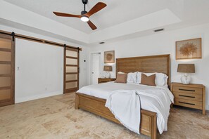 Ein Schlafzimmer mit einem hölzernen Bett, einem Deckenventilator, einem Nachttisch mit Lampe und einer Tür mit Schiebevorrichtung.