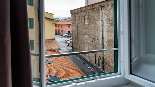 Una ventana que da a un edificio con un campanario, una calle con coches aparcados y un cielo despejado.