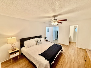 A bedroom with a bed, a nightstand, a ceiling fan, and a view of a hallway and bathroom. - Grand Deluxe Bay 3BR Penthouse near Disney (Kissimmee)