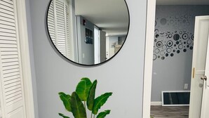 Un pasillo con un espejo redondo, una planta en maceta y un papel tapiz estampado.