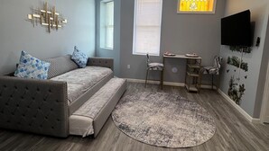 Une chambre moderne avec un canapé-lit, un bureau, une chaise, un tapis rond et un téléviseur fixé au mur.