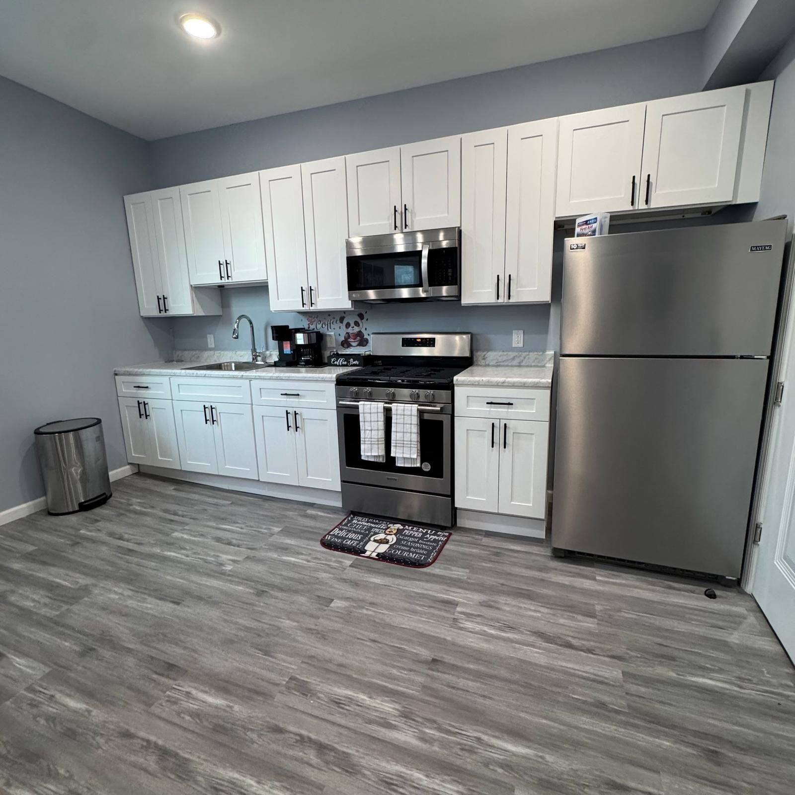 Una cocina moderna con armarios blancos, electrodomésticos de acero inoxidable y suelo gris.