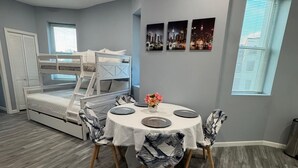 Une pièce avec des lits superposés, une table à manger avec des chaises et une fenêtre avec des stores.